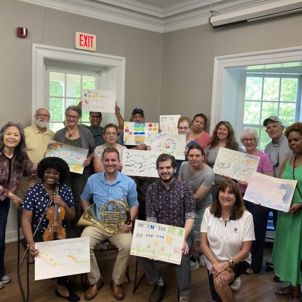 A group of people posing for photo, holding up artwork they have done.