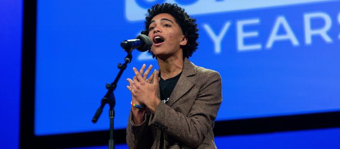 A young woman with her hands upraised speaks into a microphone