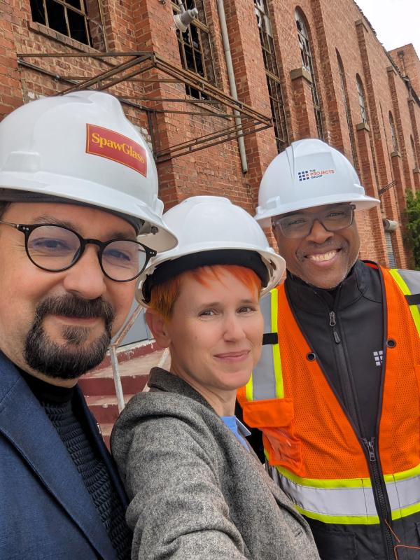 Three people standing and smiling with white hard hats on their heads.